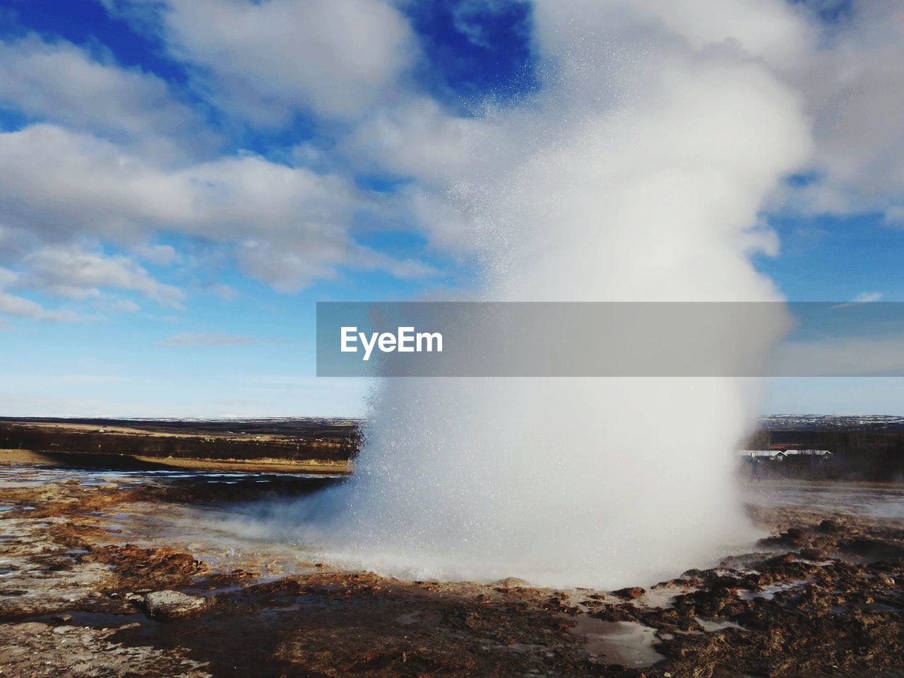 Geyser spraying water against cloudy sky