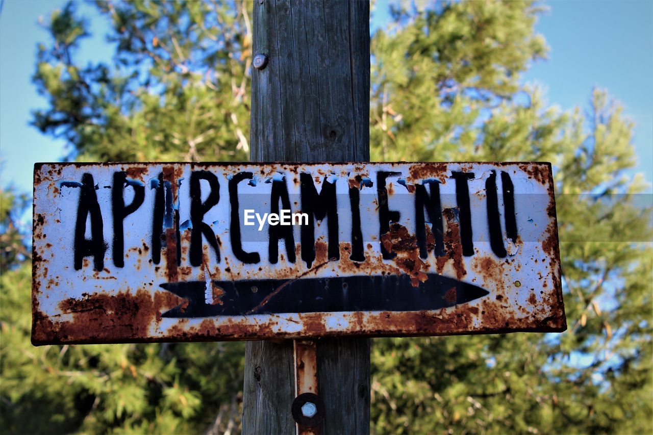 communication, sign, text, tree, plant, no people, wood, nature, western script, day, guidance, focus on foreground, outdoors, close-up, blue, street sign, information sign, rusty, metal, sky, signage