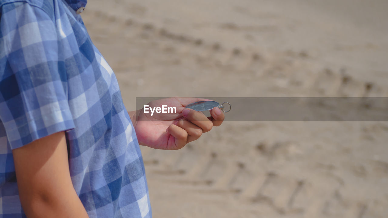 Midsection of man holding navigational compass at beach