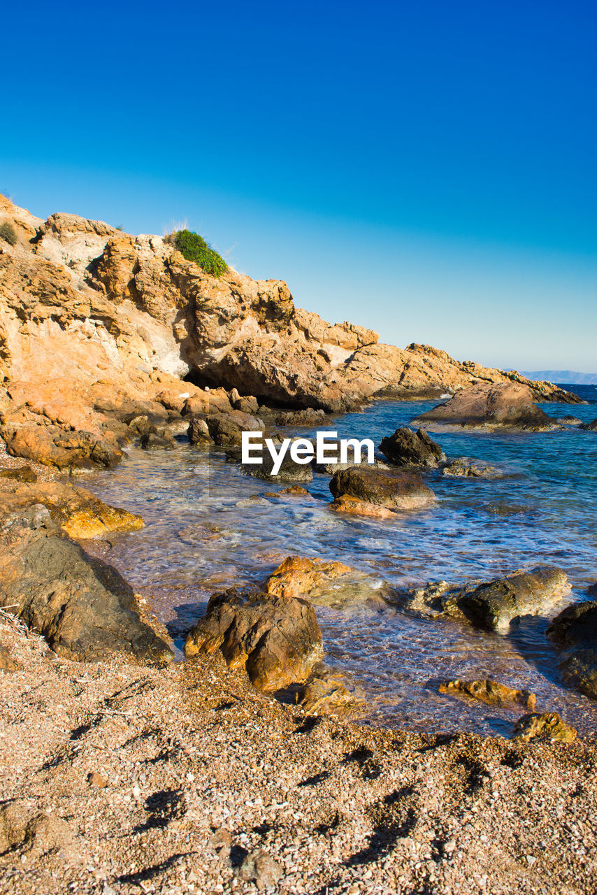 Rocks in sea against clear blue sky