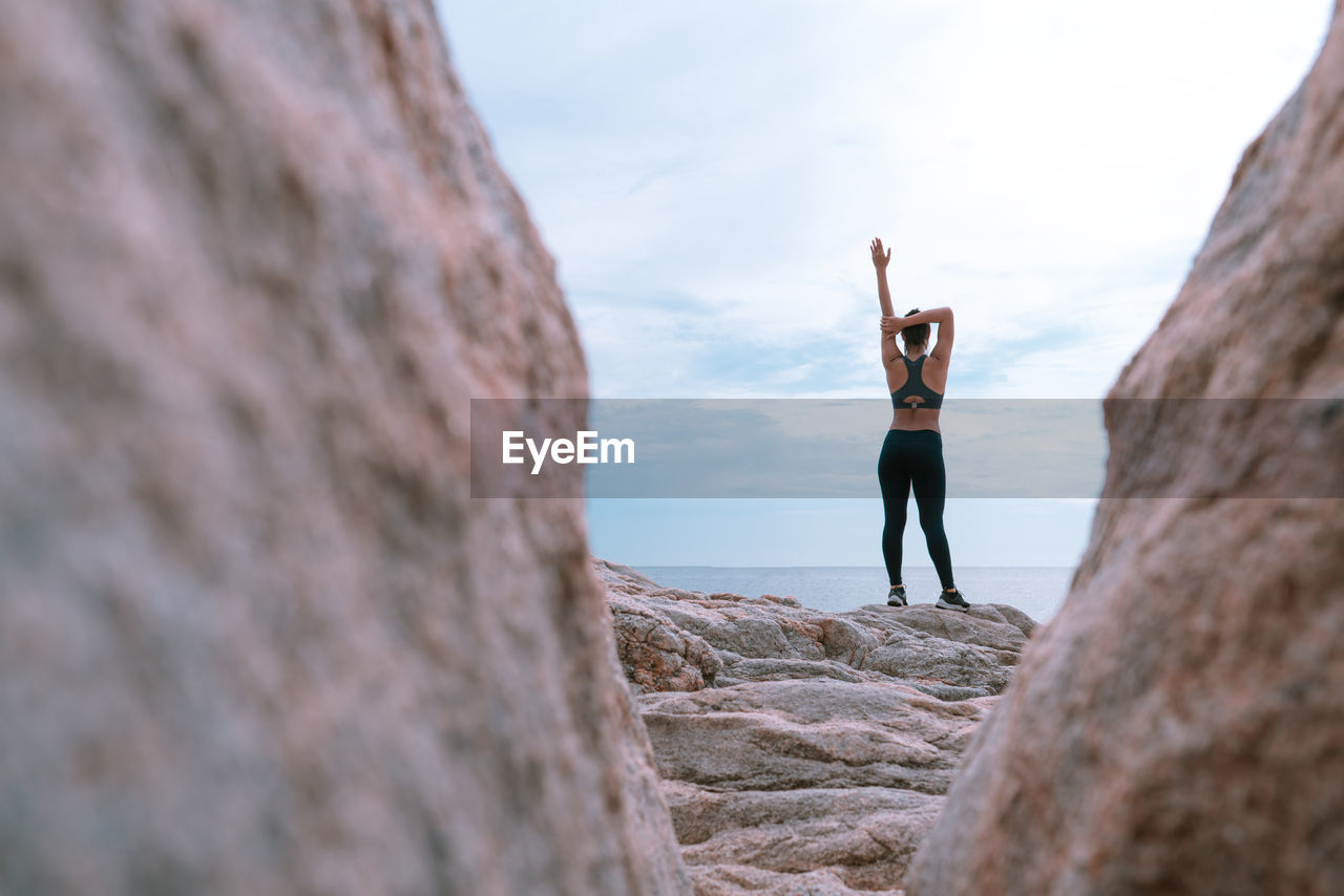 Full length rear view of woman exercising on rock at beach