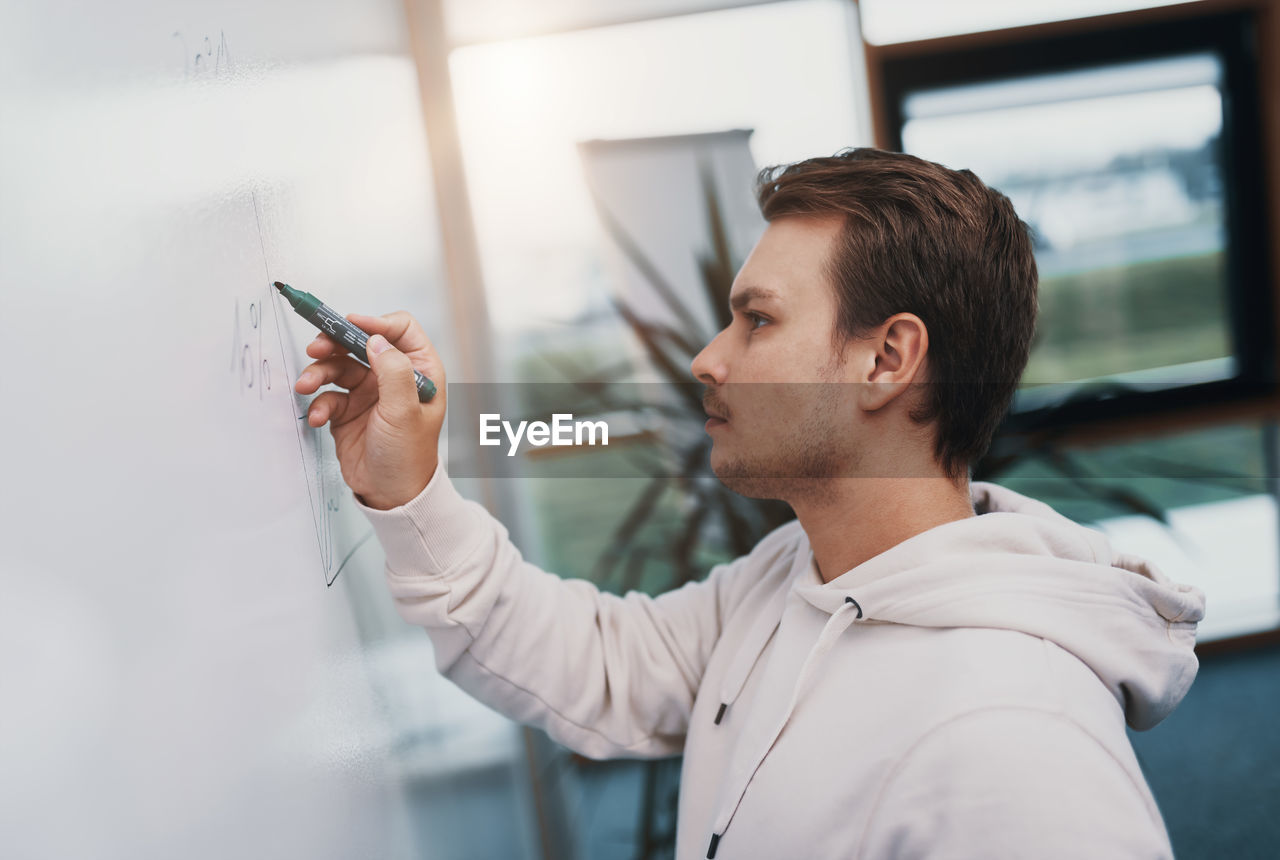 Young business man writes on a whiteboard, he is busy and works hard in his start up company