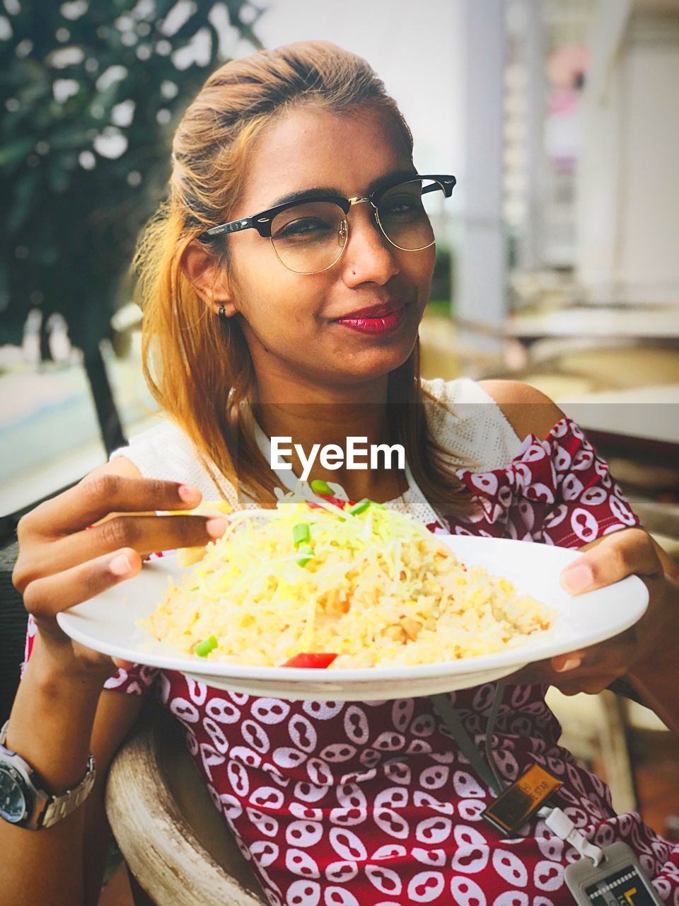 Portrait of young woman holding rice in plate while sitting on chair