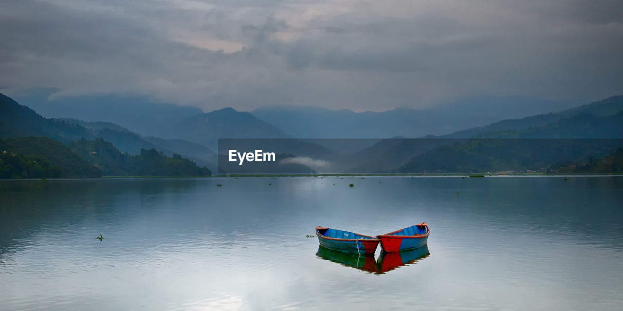 Rowboat moored in lake by mountains against cloudy sky