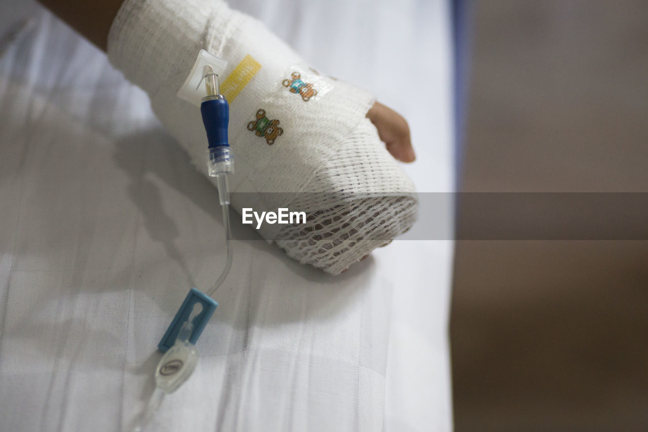 Cropped image of child with hand wrapped in bandage on bed at hospital