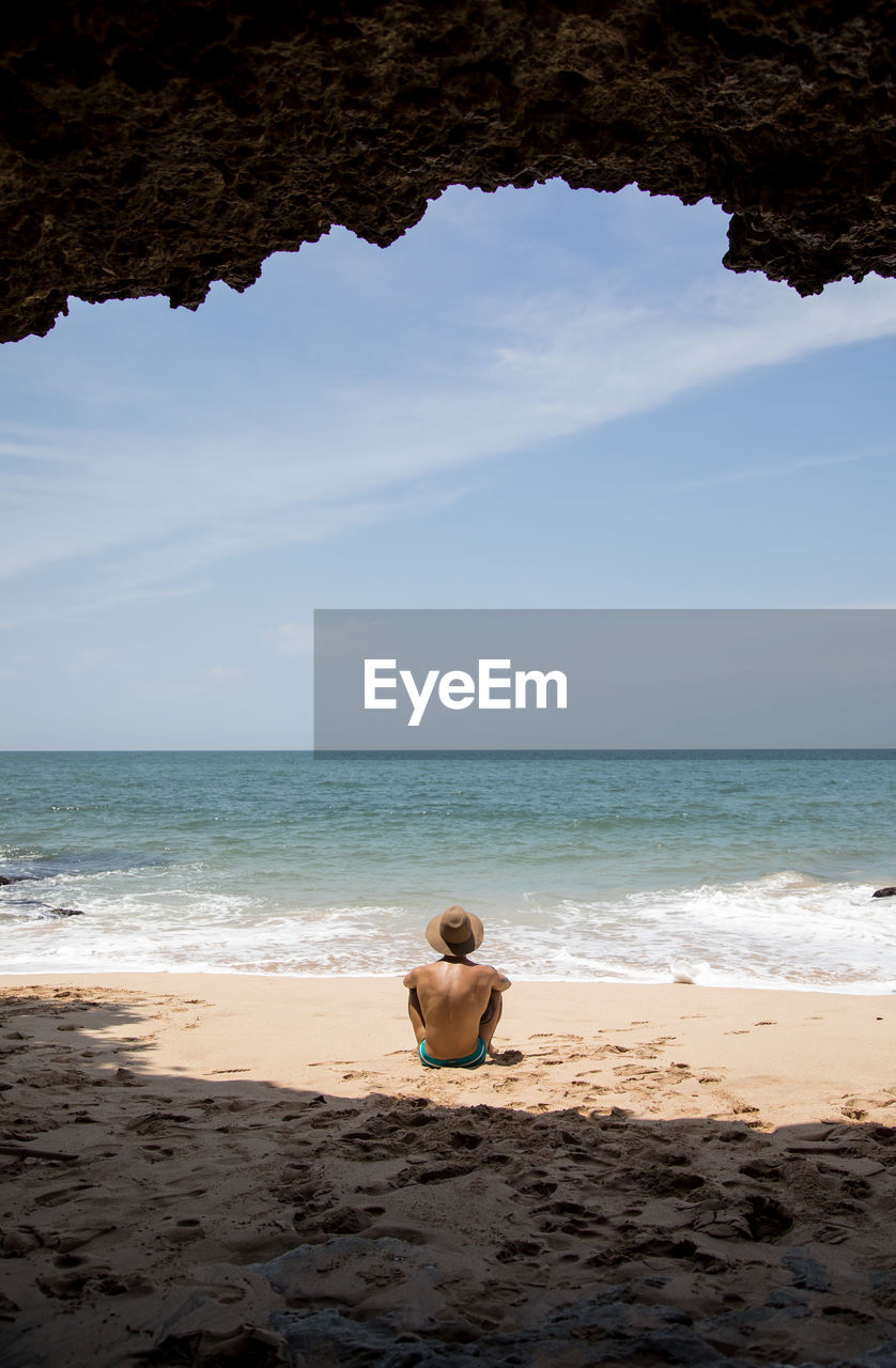 Rear view of shirtless man sitting on beach