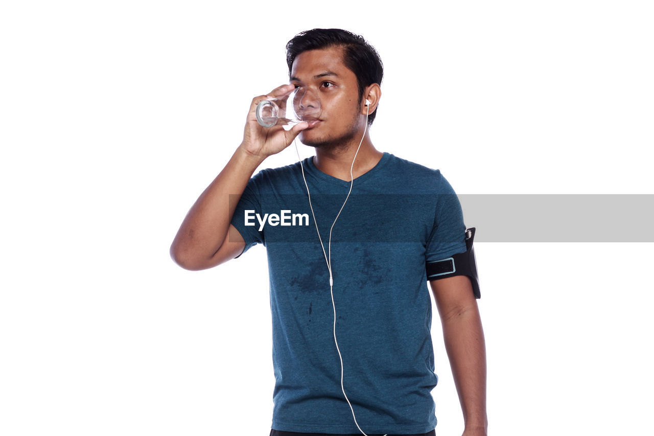 Young man drinking water while standing against white background