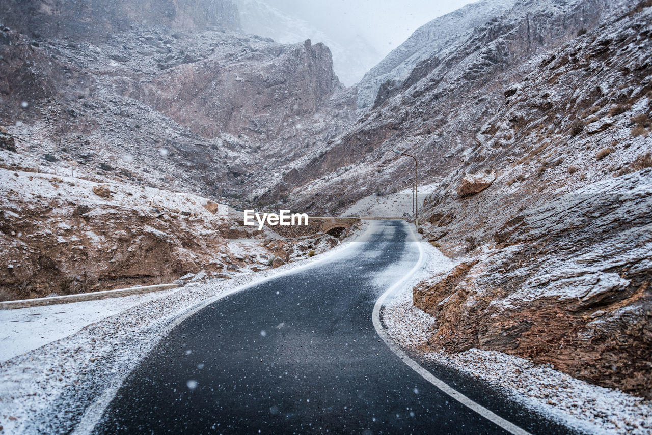 Snow covered road by mountain against sky