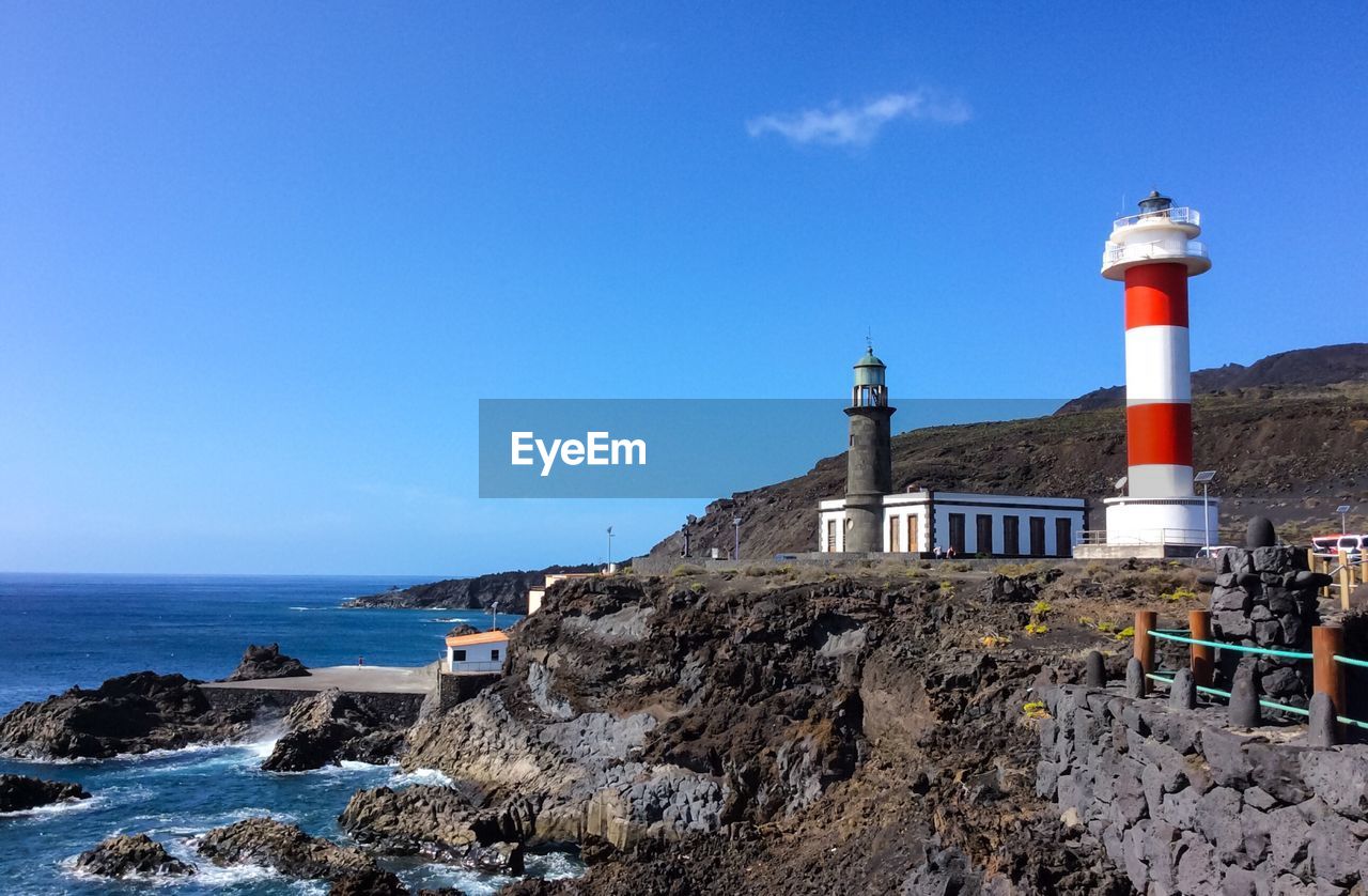 Lighthouse on beach by building against sky