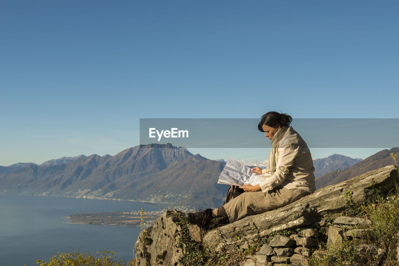 Side view of female hiker with map sitting on cliff against swiss alps