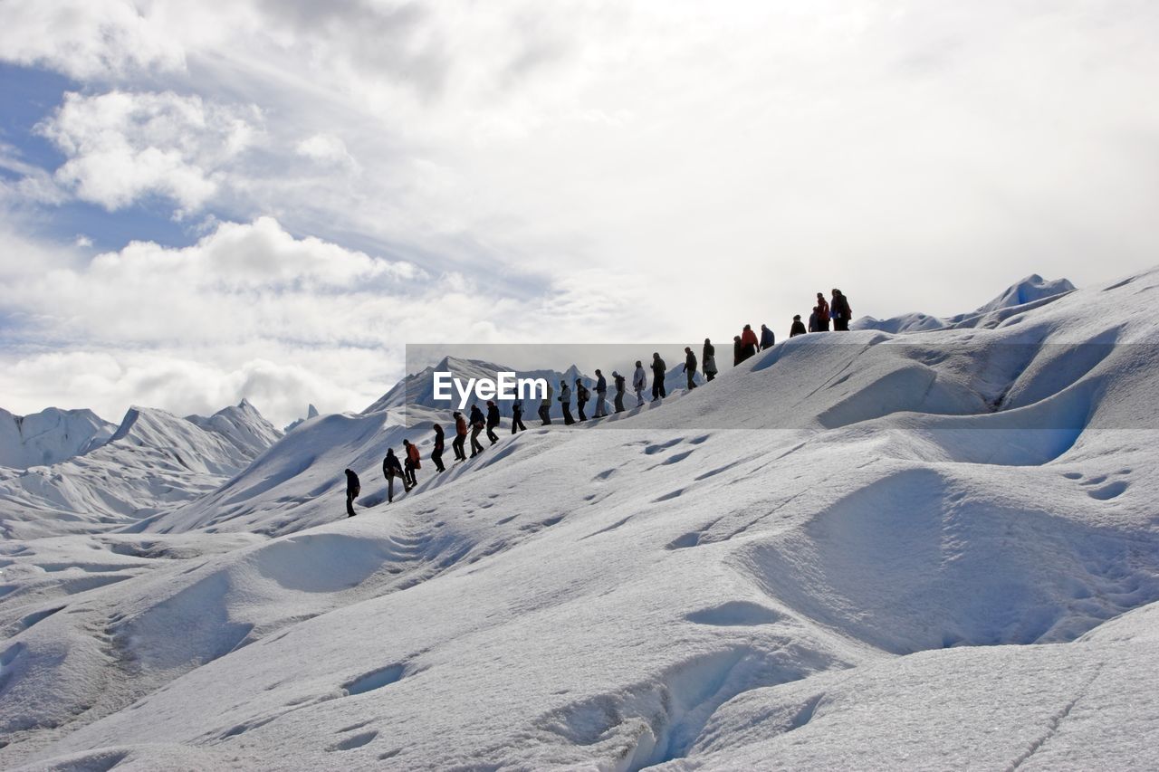 Low angle view of hikers on snowcapped mountain against sky