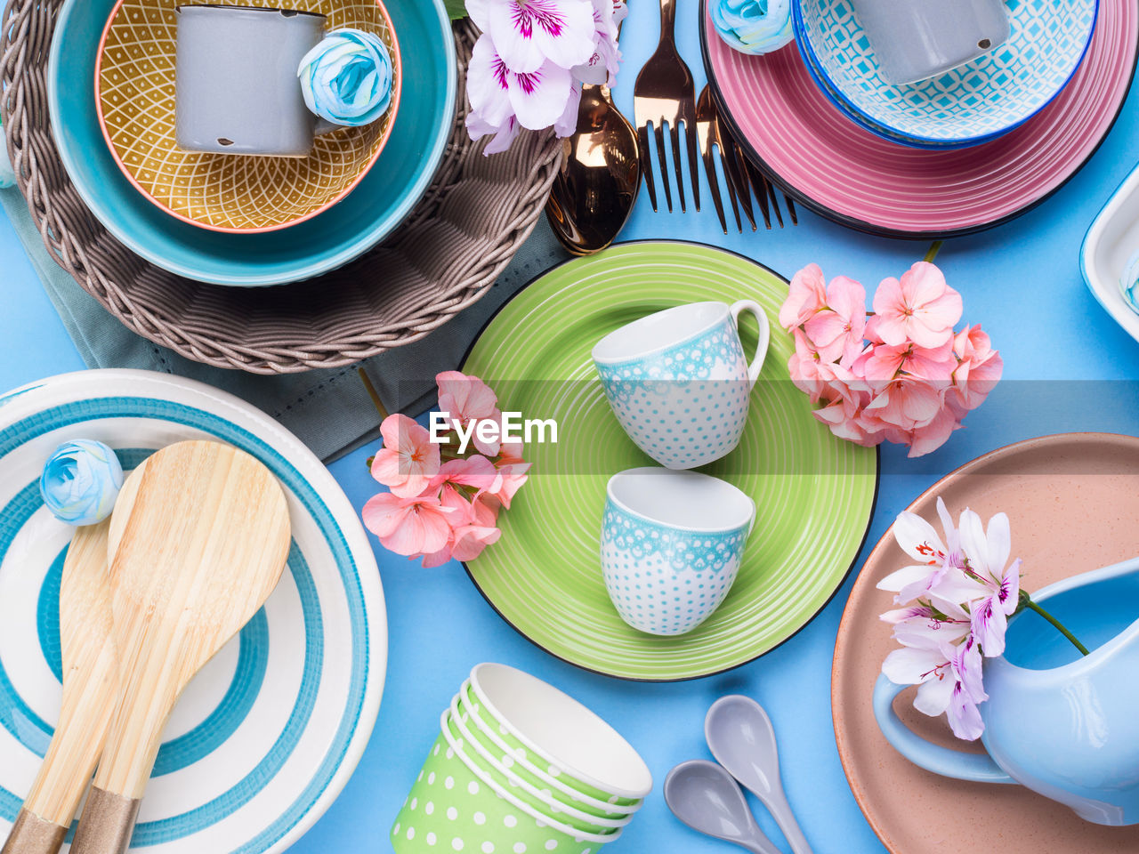 Tableware dish set on blue pastel background with flowers. flat lay