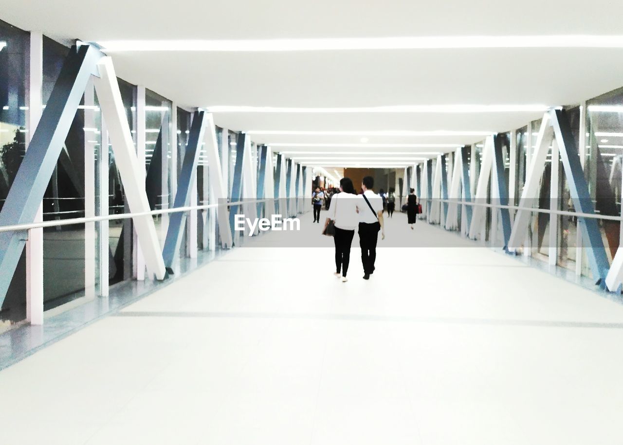 REAR VIEW OF MEN WALKING ON FOOTBRIDGE