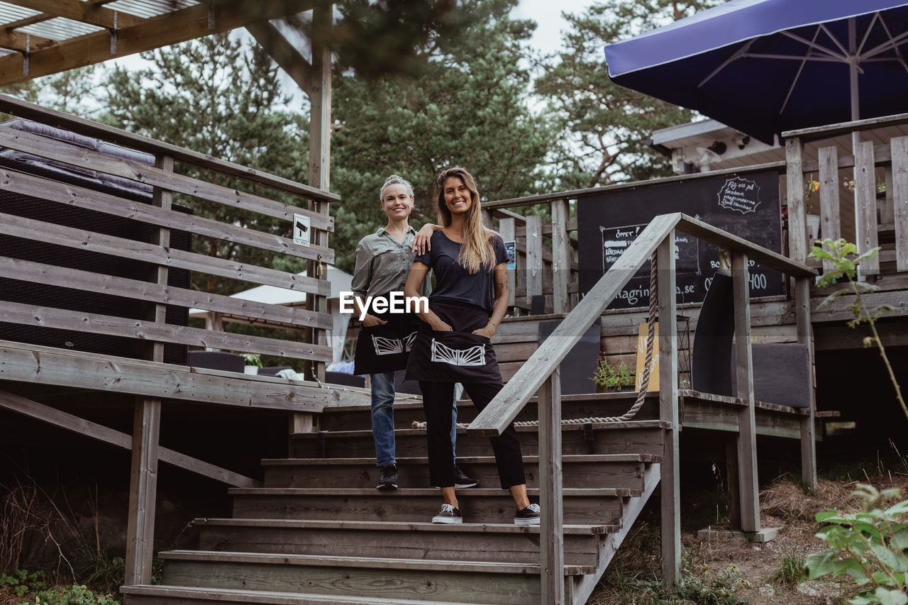 Full length portrait of smiling coworkers standing on steps in restaurant