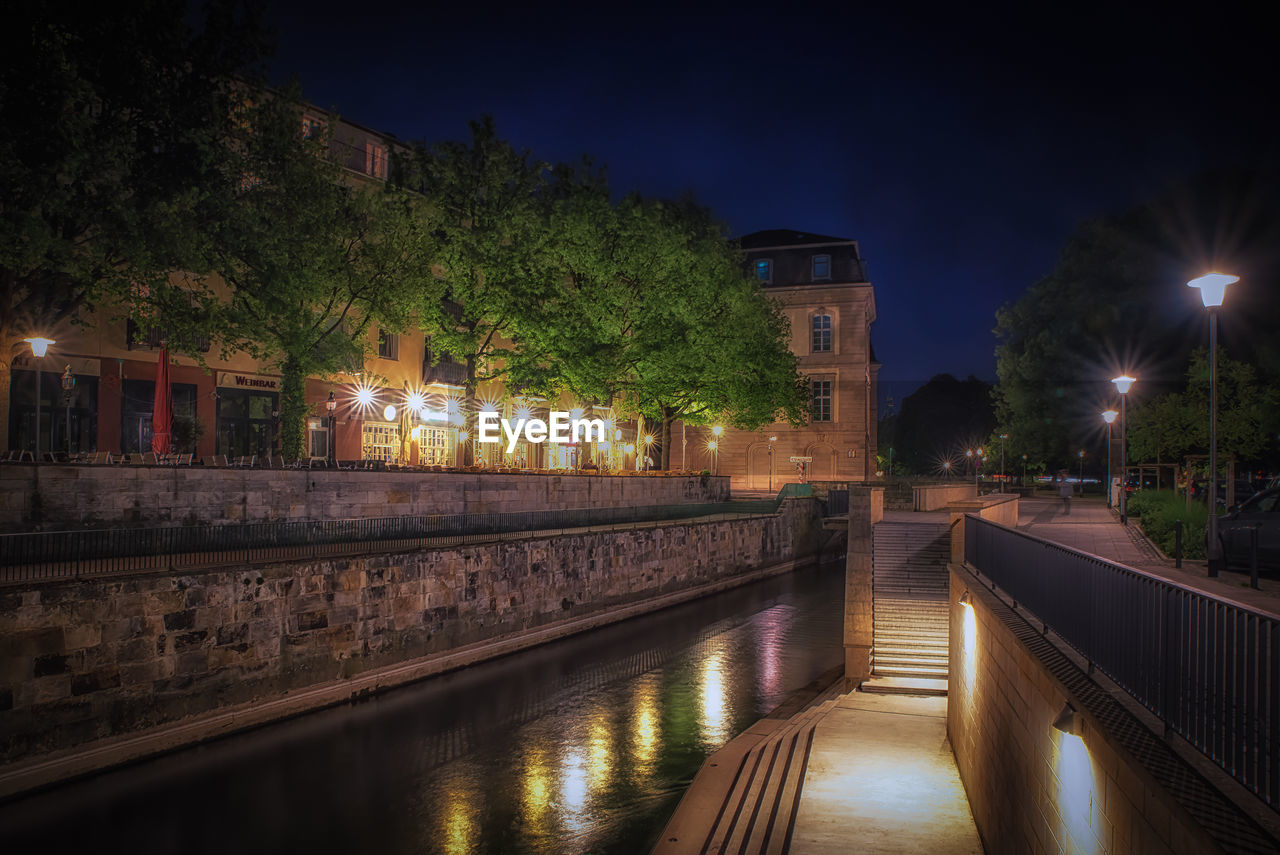 VIEW OF ILLUMINATED CANAL BY BUILDINGS AGAINST SKY