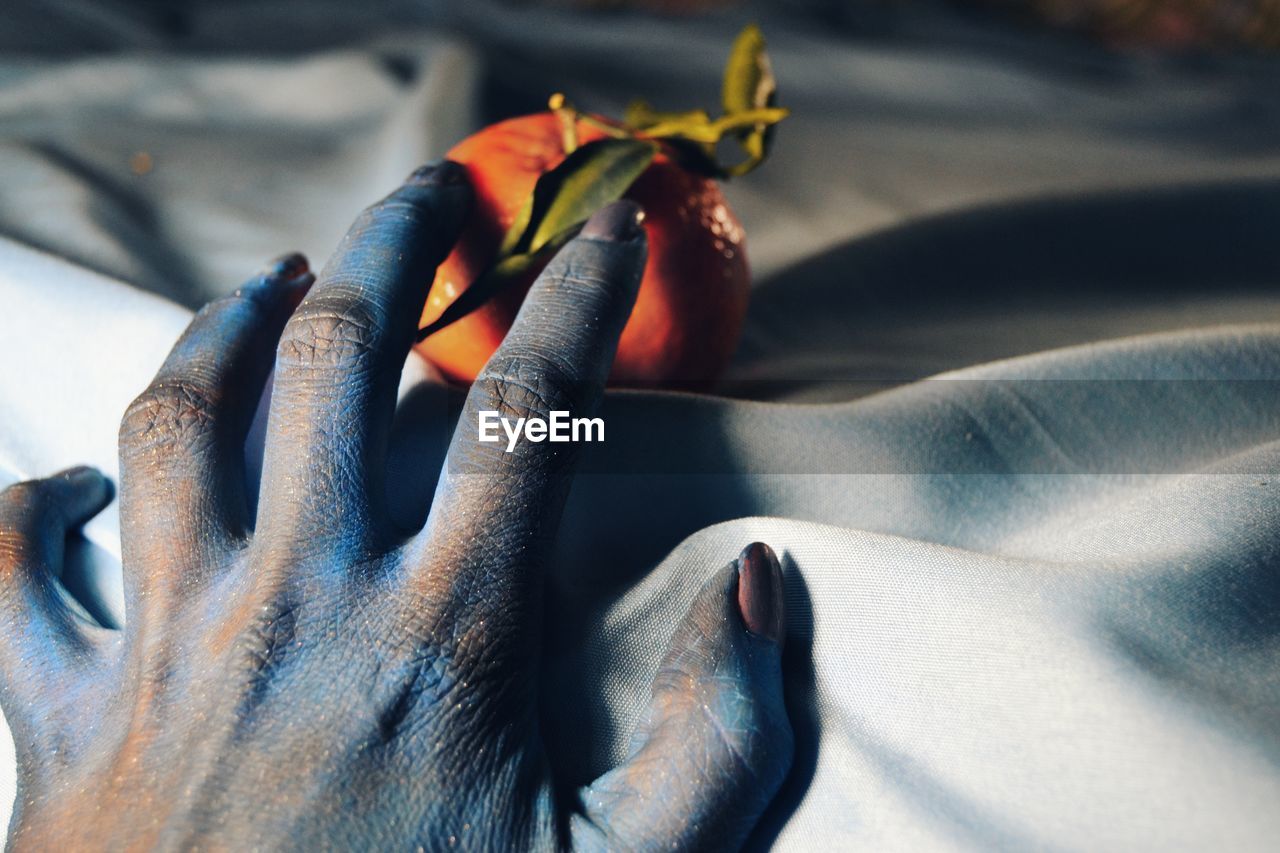 Cropped messy hand of woman with orange on bed sheet