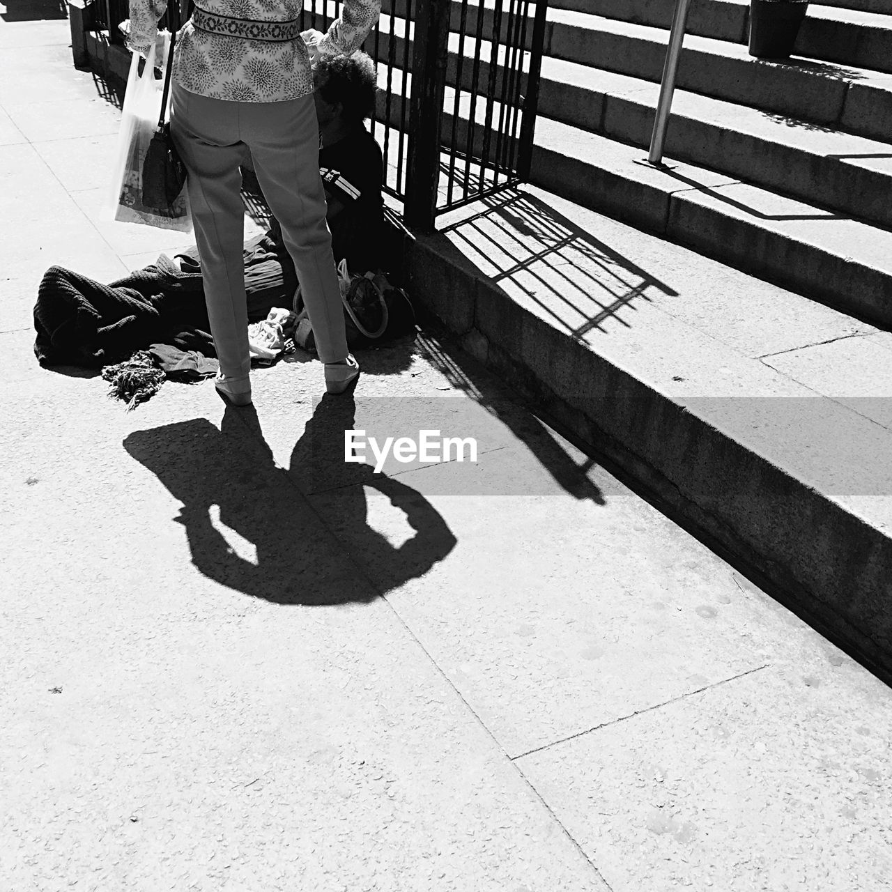 Low section of woman standing by homeless man sitting on sidewalk