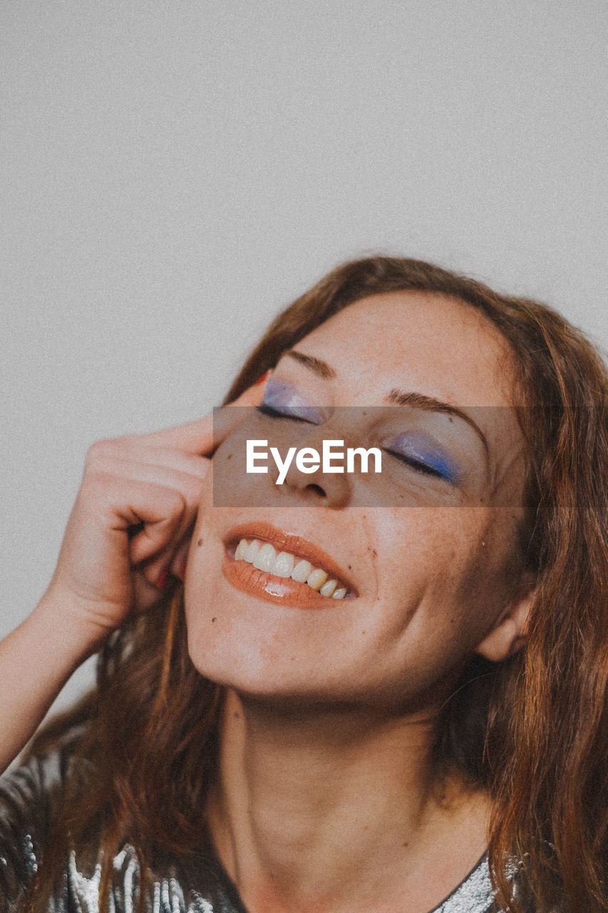 Smiling young woman with eye make-up against wall