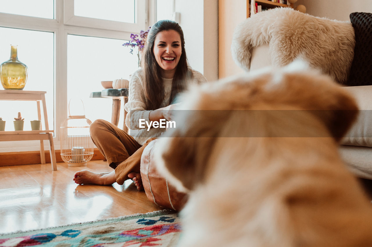 Happy woman looking at dog while sitting on floor