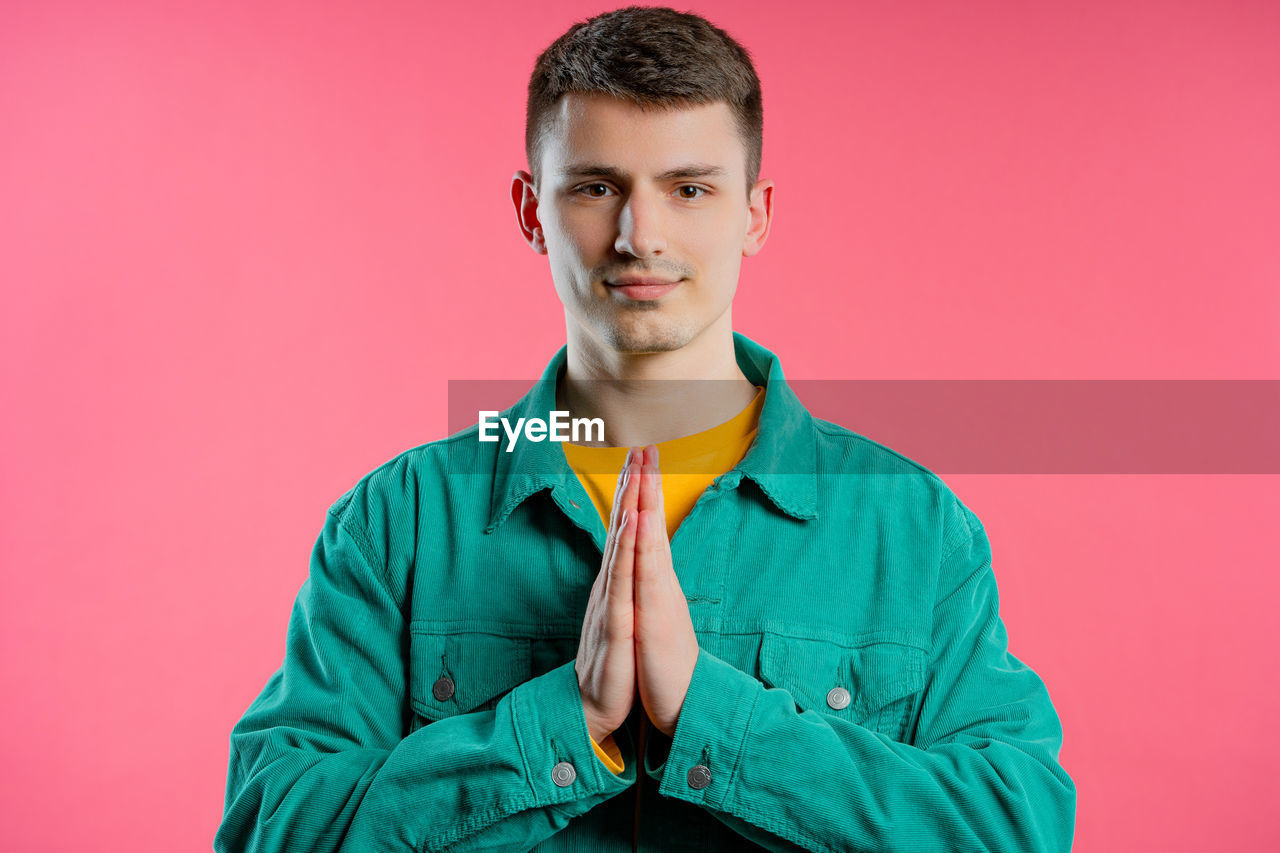 portrait, one person, studio shot, colored background, young adult, looking at camera, front view, indoors, adult, outerwear, men, sleeve, waist up, clothing, photo shoot, emotion, person, smiling, hood, pink background, casual clothing, copy space, brown hair, happiness, headshot, standing, pink, serious, individuality