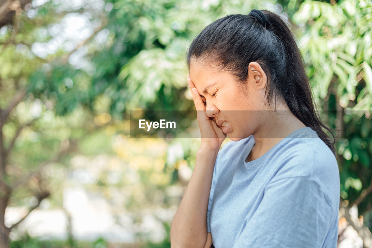 Side view of woman touching head in pain against trees