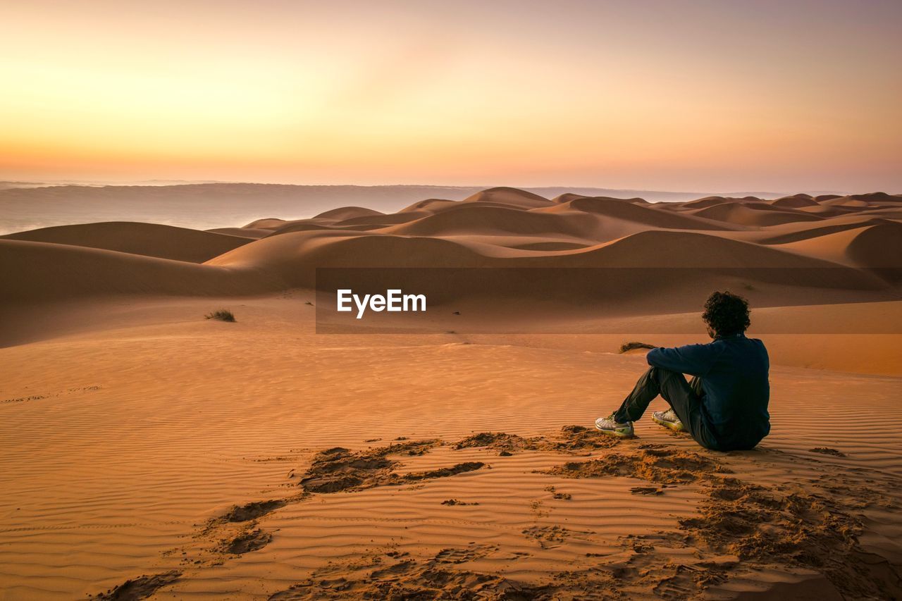 Man on sand dune in desert against sky during sunset