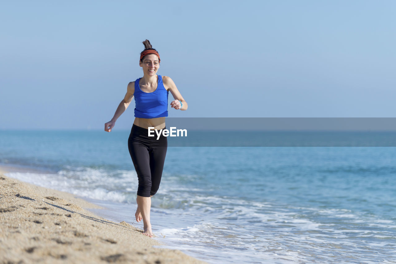 Woman running at beach against clear blue sky