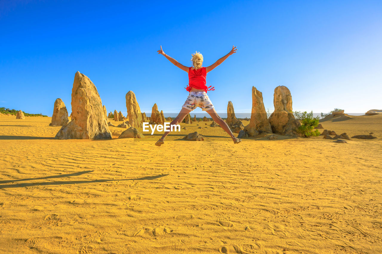 Rear view of woman with arms outstretched jumping against sky