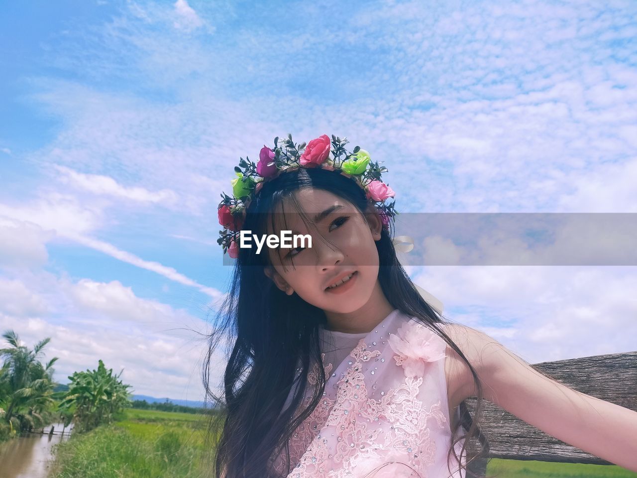 Portrait of beautiful woman with red flower against sky