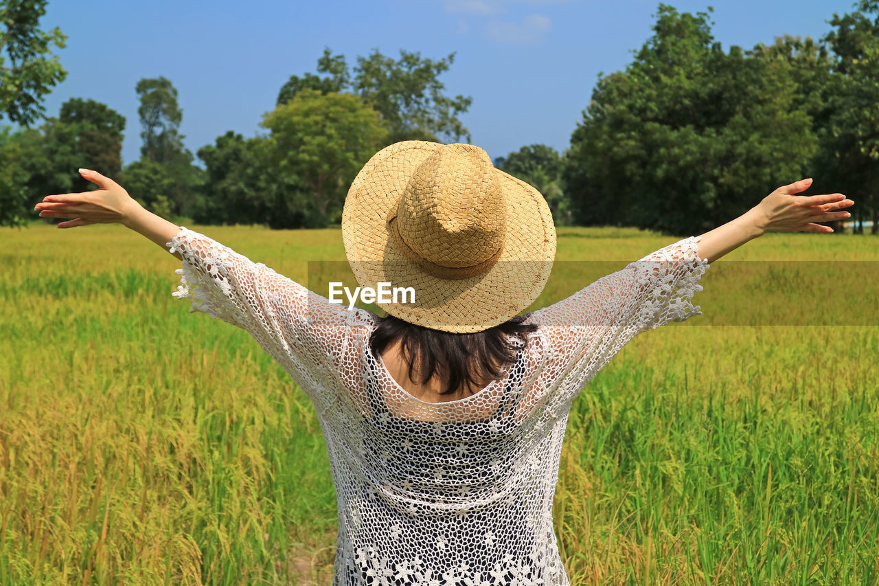 Rear view of woman with arms outstretched standing on field