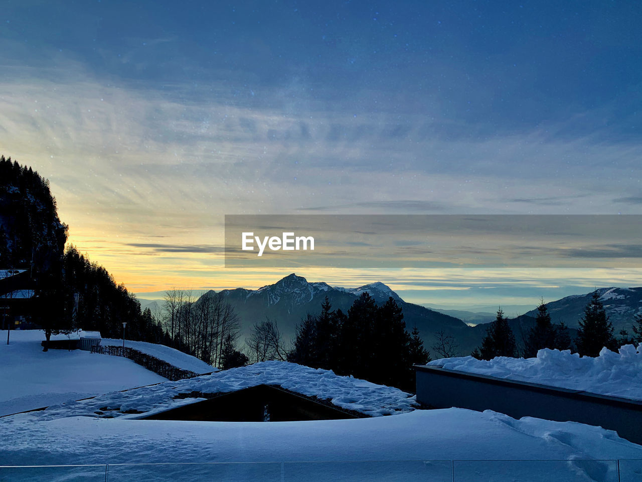 Snow covered landscape against sky during sunset