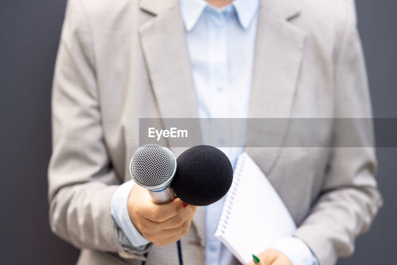 Female journalist at news conference or media event, writing notes, holding microphone