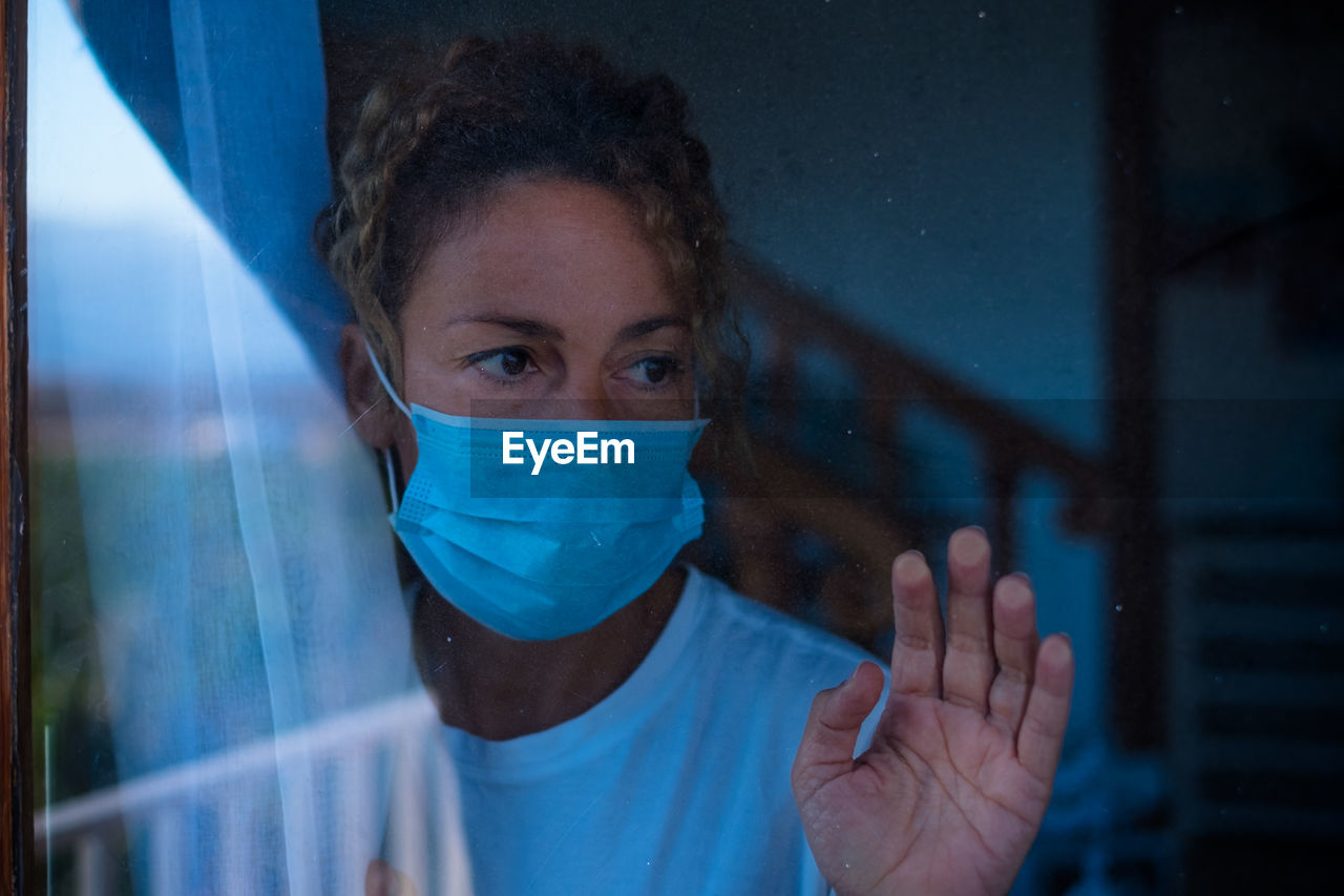 Close-up of woman wearing mask seen through window