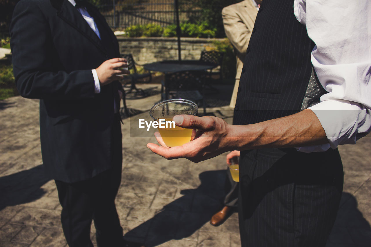 Midsection of men holding drink in glass while standing outdoors