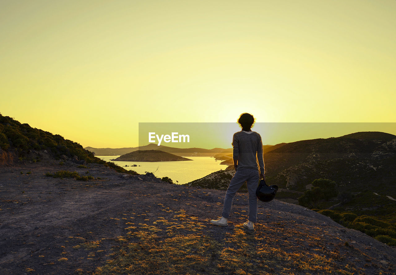 REAR VIEW OF MAN WALKING ON MOUNTAIN AGAINST SKY