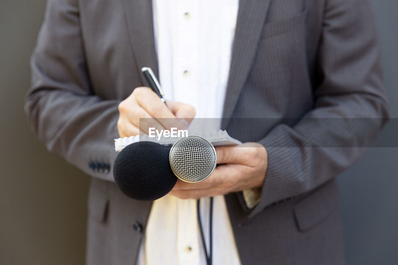 Journalist at press conference or media event, writing notes, holding microphone