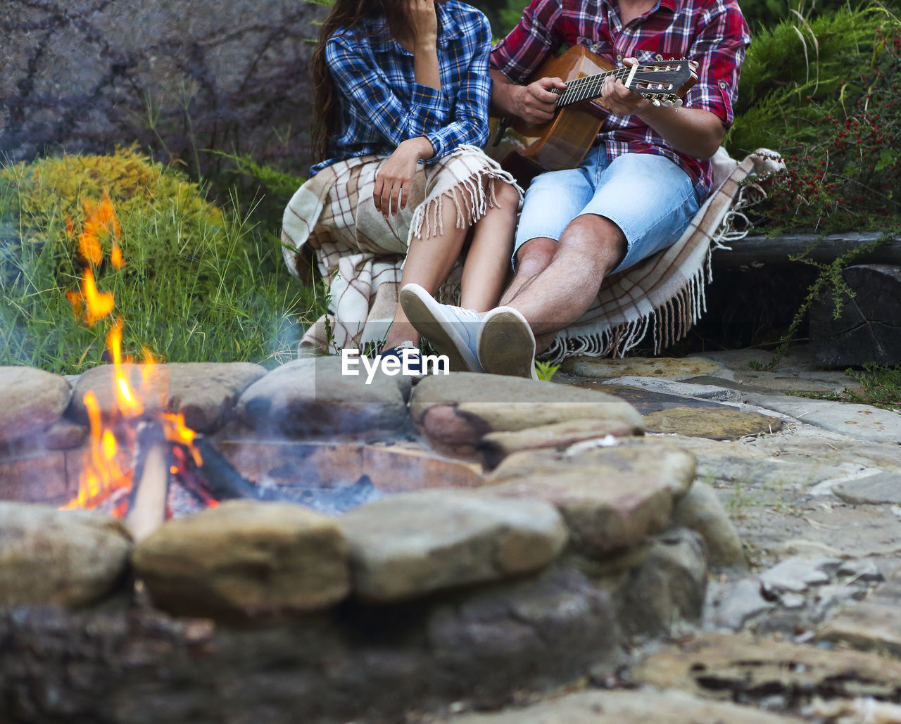 Low section of man playing guitar while sitting with girlfriend outdoors