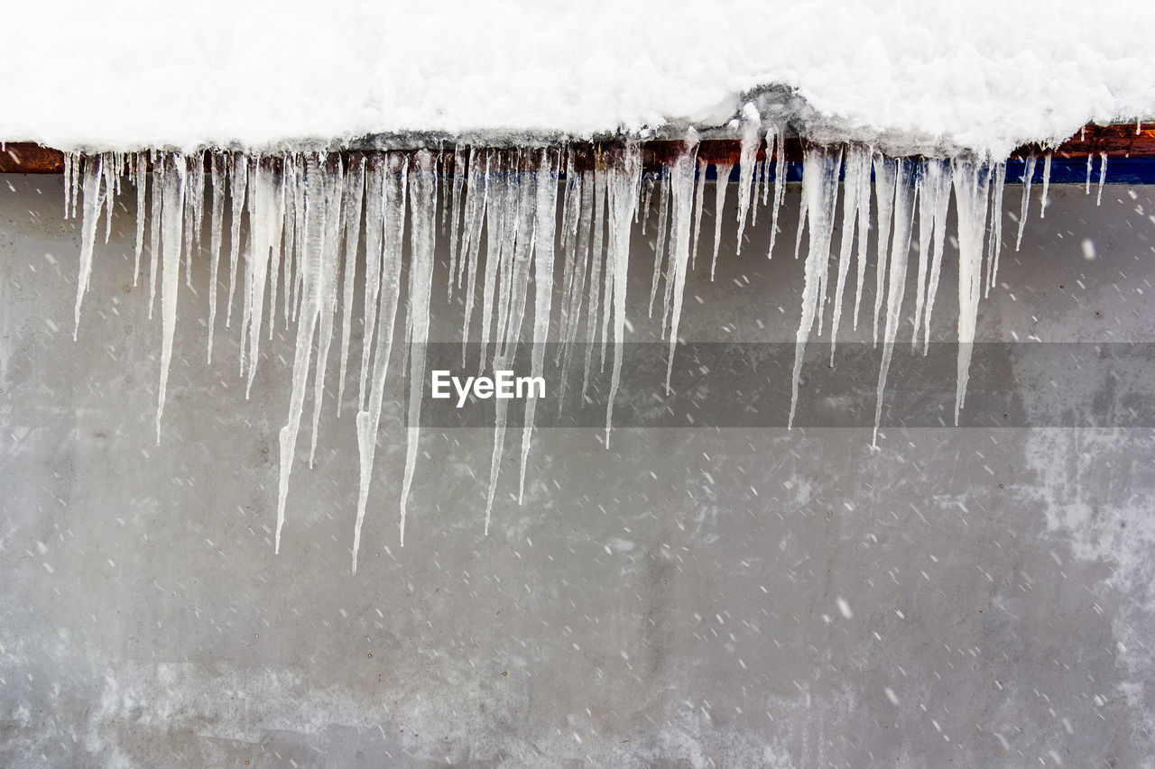 Icicles hanging from the roof against the gray wal