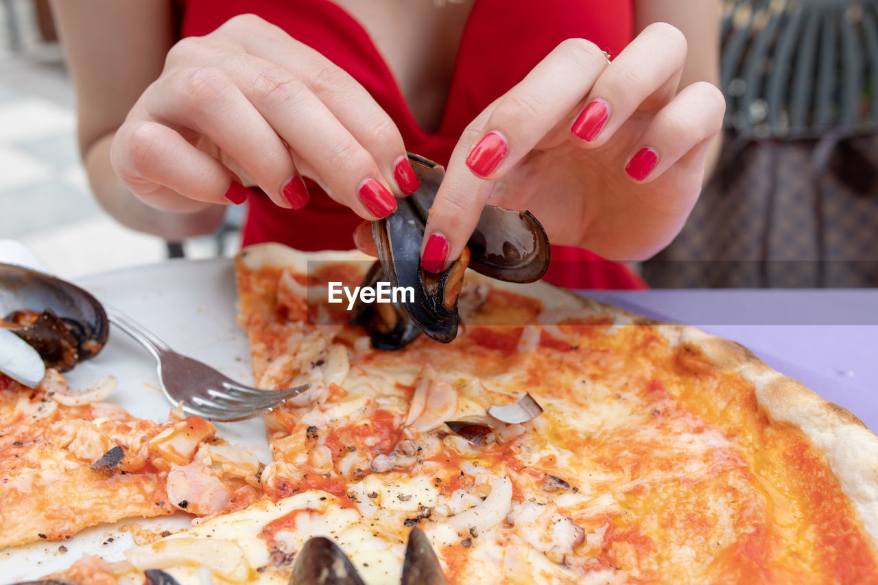 Midsection of woman holding mussels over pizza over table at restaurant 