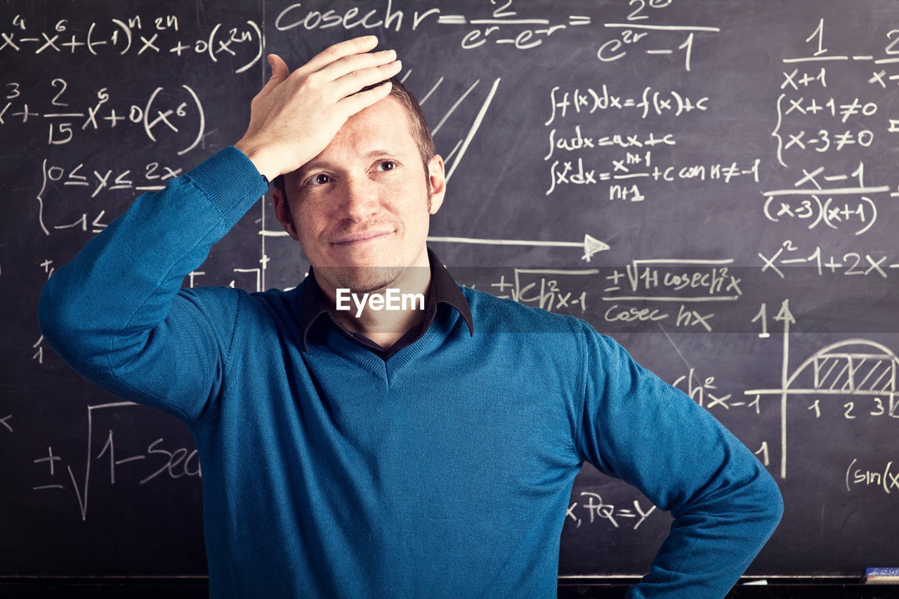 Frustrated teacher standing against blackboard in classroom