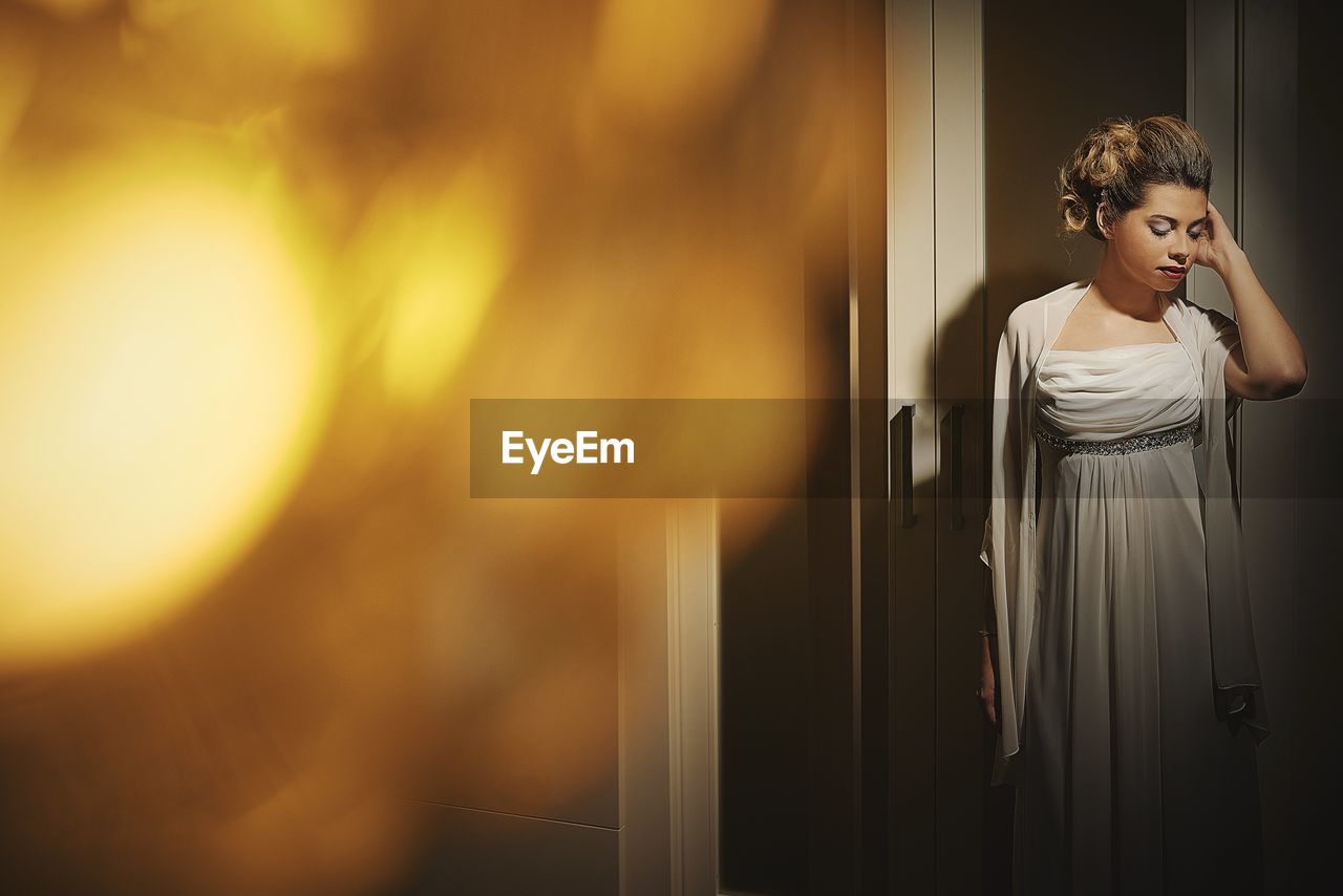 Bride wearing wedding dress while standing against cupboard