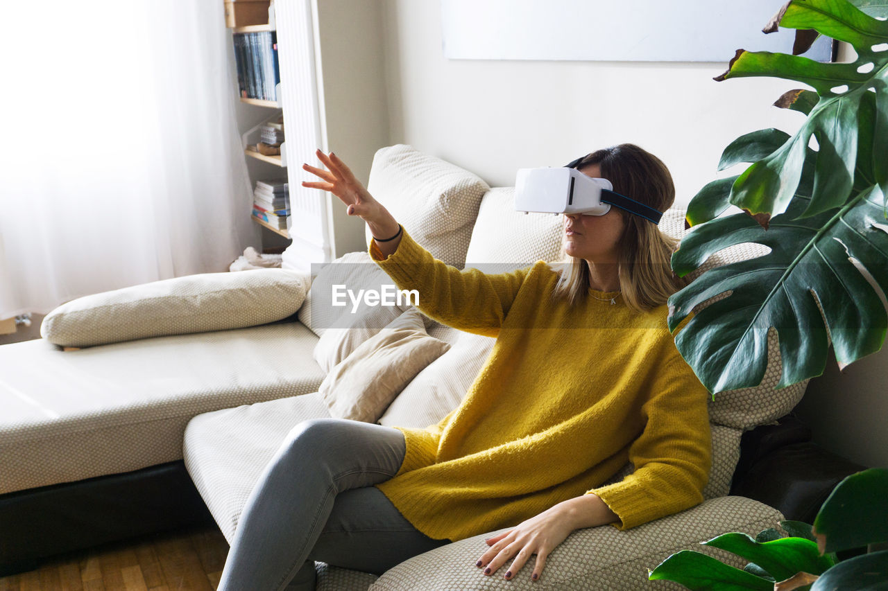 Young woman using virtual reality simulator on sofa at home