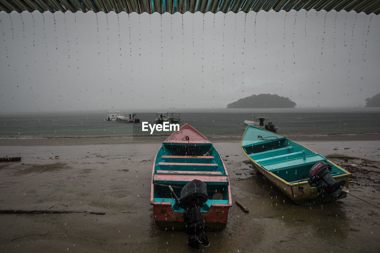 Boats moored on sand against sea during rainy season