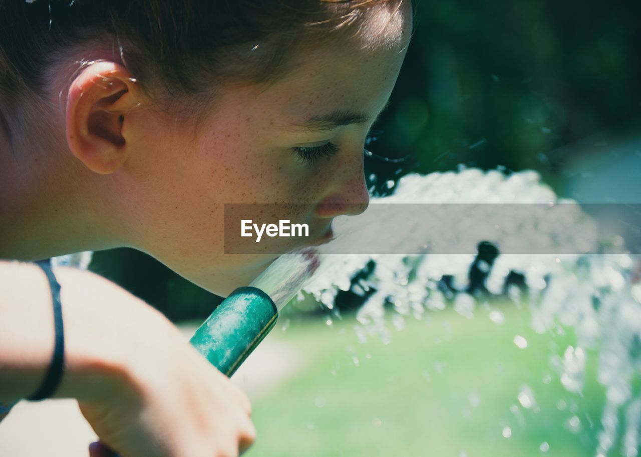 Close-up of girl drinking water from hose in yard