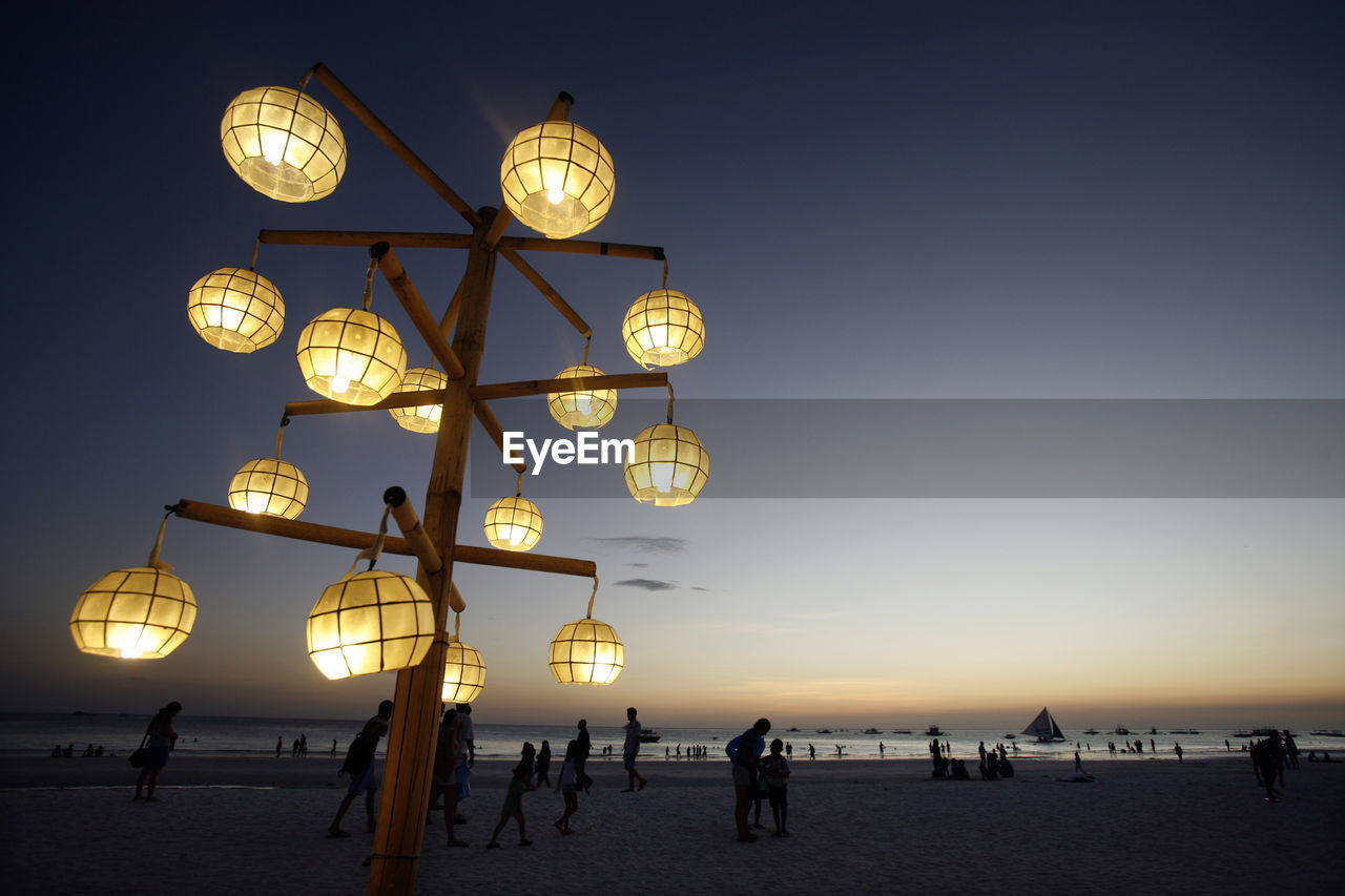Illuminated lamp post at beach against sky at dusk