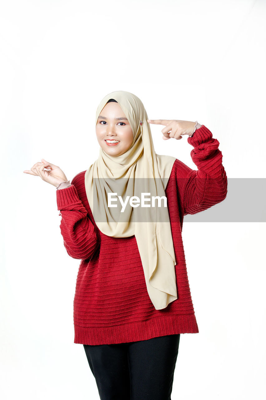 PORTRAIT OF A SMILING YOUNG WOMAN AGAINST WHITE BACKGROUND