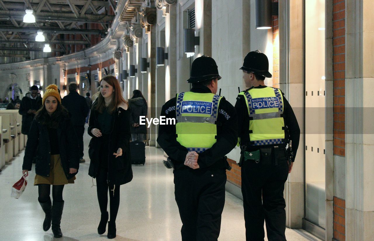 Rear view of police officers walking by women in illuminated corridor