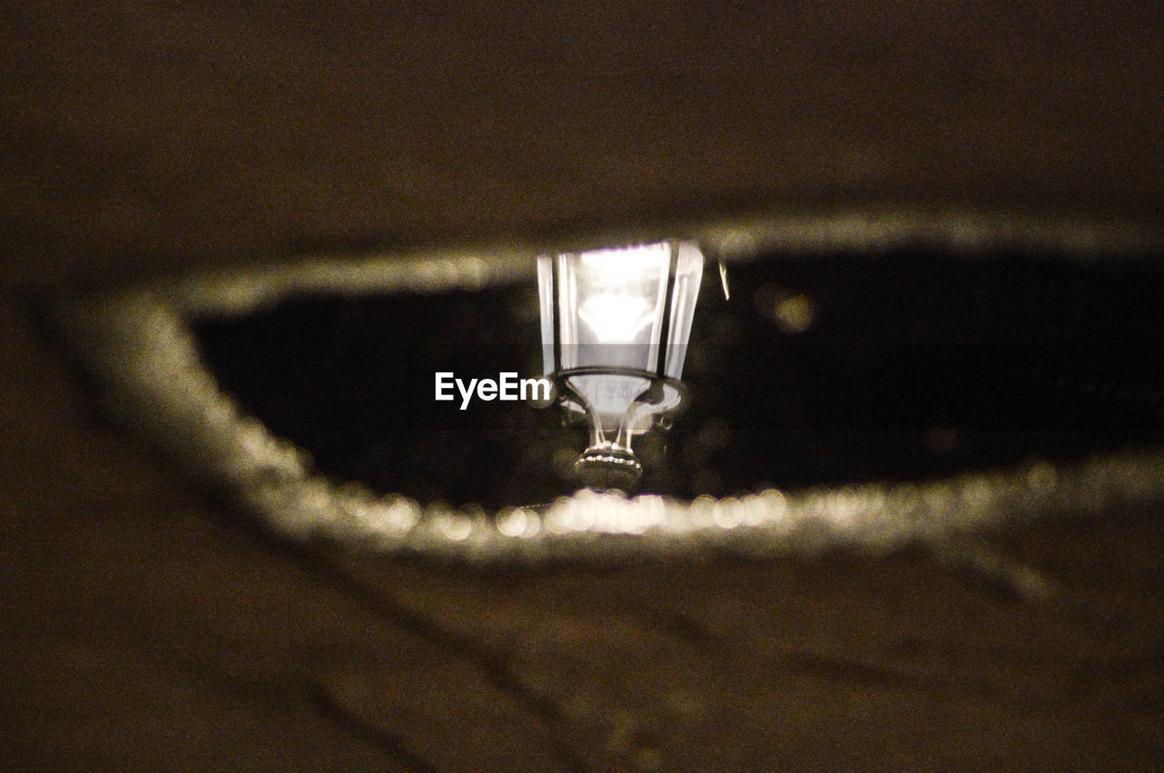 CLOSE-UP OF ILLUMINATED LAMP IN DARK ROOM