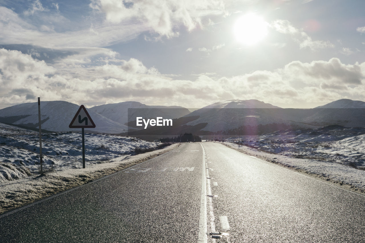 A winding road warning sign on an icy road in a snowy winter mountain scene in scotland