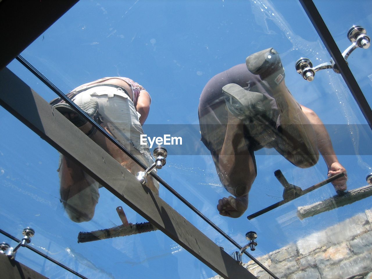 Low angle view of workers cleaning glass window against clear sky